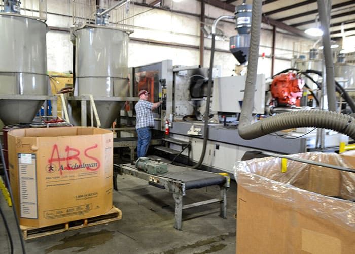 Operator at an injection molding machine beside material hoppers and a box of ABS resin