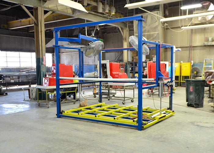 Blue and yellow steel fixture on the shop floor with red molds behind it