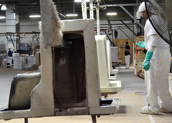 Technician in a protective suit beside a tub mold with raw fiberglass at its edges