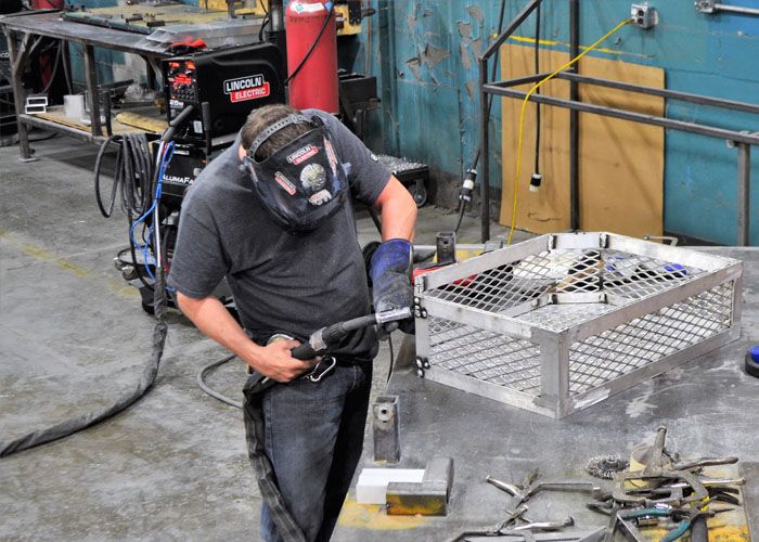 Welder in a hood working on an aluminum basket